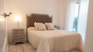 A bedroom with a tufted headboard, a bed with a quilted bedspread, two bedside tables, and a nightstand. - Cozy Apartment by the Sea in Carboneras (Carboneras)