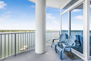 A balcony with a view of the water, a white column, and two blue chairs.