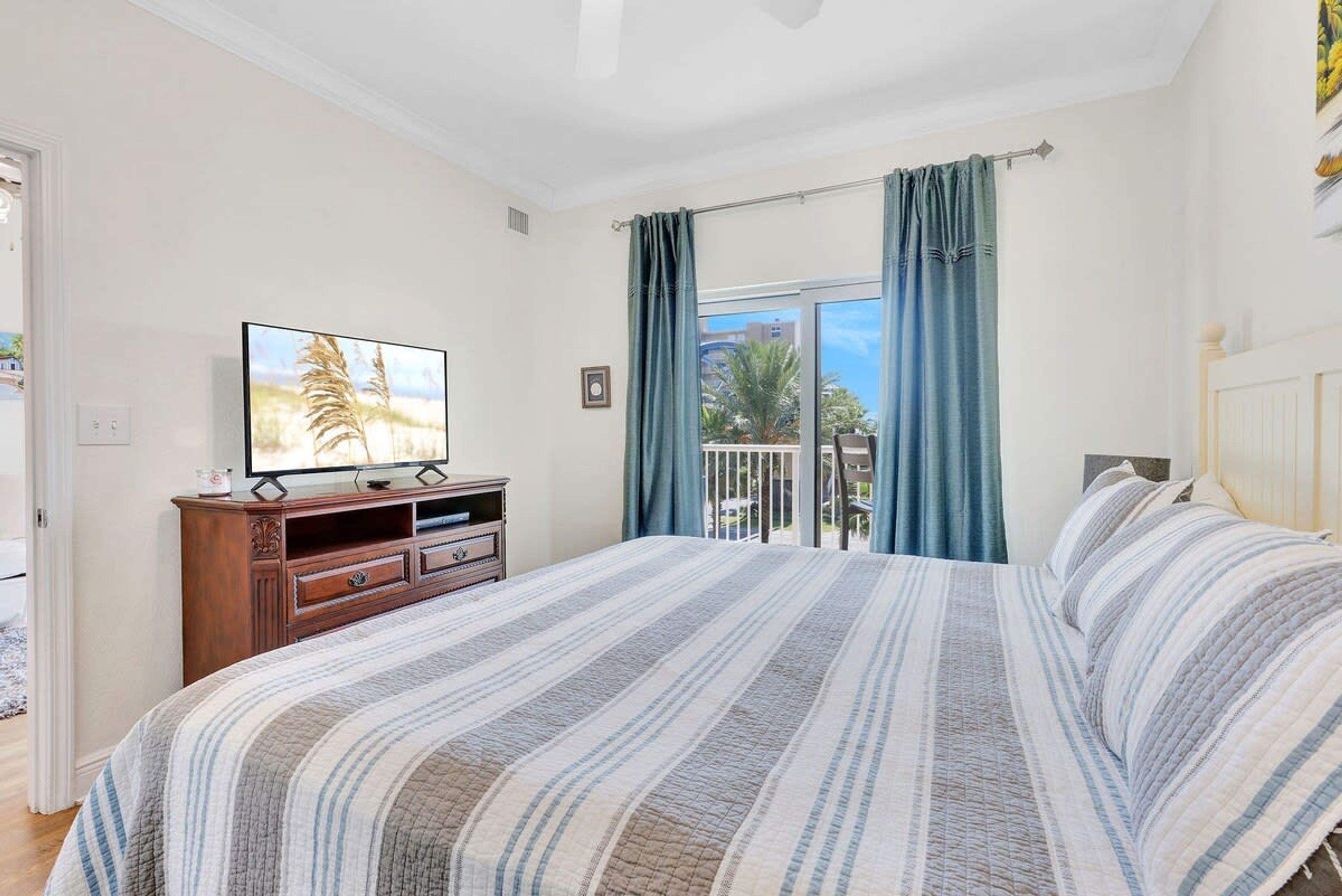 A bedroom with a bed, a TV on a wooden cabinet, and a balcony with curtains.