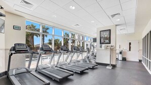A gym with treadmills, a digital clock, and large windows with a view of palm trees.