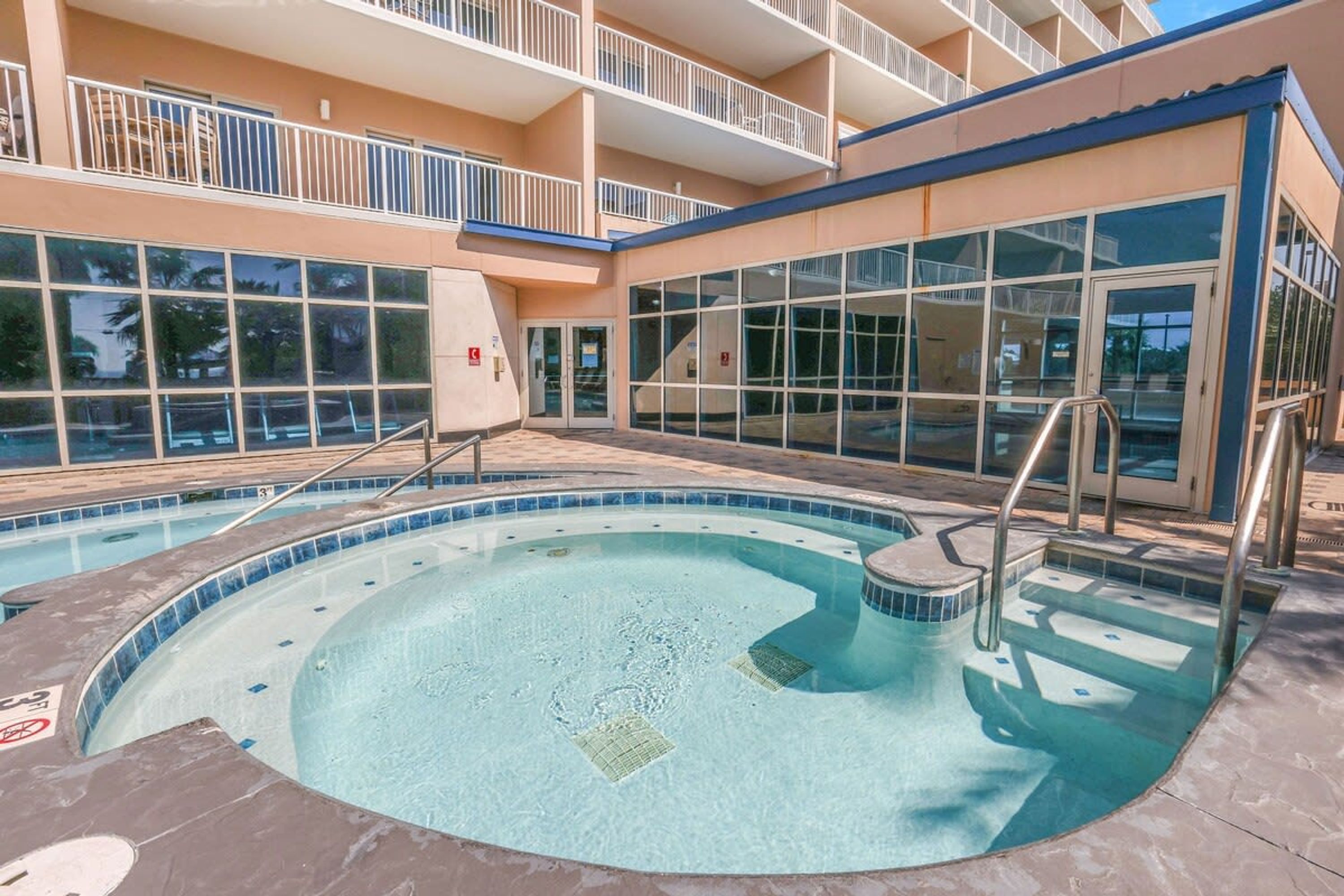 A swimming pool with a glass enclosure, surrounded by a building with balconies and large windows.