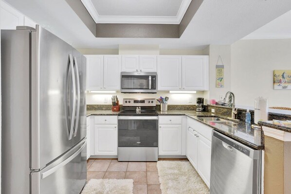 A modern kitchen with stainless steel appliances, white cabinetry, and a granite countertop. - Crystal Tower 206- Amenities Galore Lazy River (Gulf Shores)
