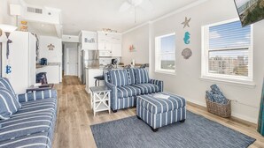 A modern living room with a sofa, ottoman, and a dining area with a table and chairs. - Tradewinds 1301 Beachfront Top-floor (Orange Beach)