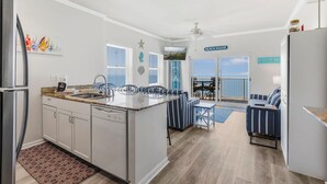 A modern kitchen with a central island, white cabinetry, and a dining area with striped chairs. - Tradewinds 1301 Beachfront Top-floor (Orange Beach)