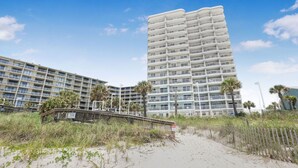 A beachfront hotel with multiple balconies, a sandy beach area, and a wooden walkway leading to the entrance. - Tradewinds 1301 Beachfront Top-floor (Orange Beach)