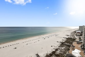 A beach with a row of parked cars, a flag, and a building with a pool area. - Tradewinds 1301 Beachfront Top-floor (Orange Beach)