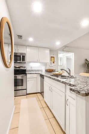 A modern kitchen with white cabinets, a granite countertop, stainless steel appliances, and a wooden-framed mirror.