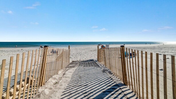 Una pasarela de madera que conduce a una playa arenosa bajo un cielo azul despejado.