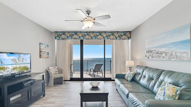 A living room with a television, a sofa, a coffee table, and a balcony with a view of the ocean. - Windward Pointe 804- Sleeps 10 Beachfront Resort Amenities (Orange Beach)