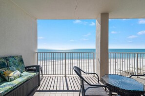 A balcony with a view of the beach, a sofa, and a table with chairs.