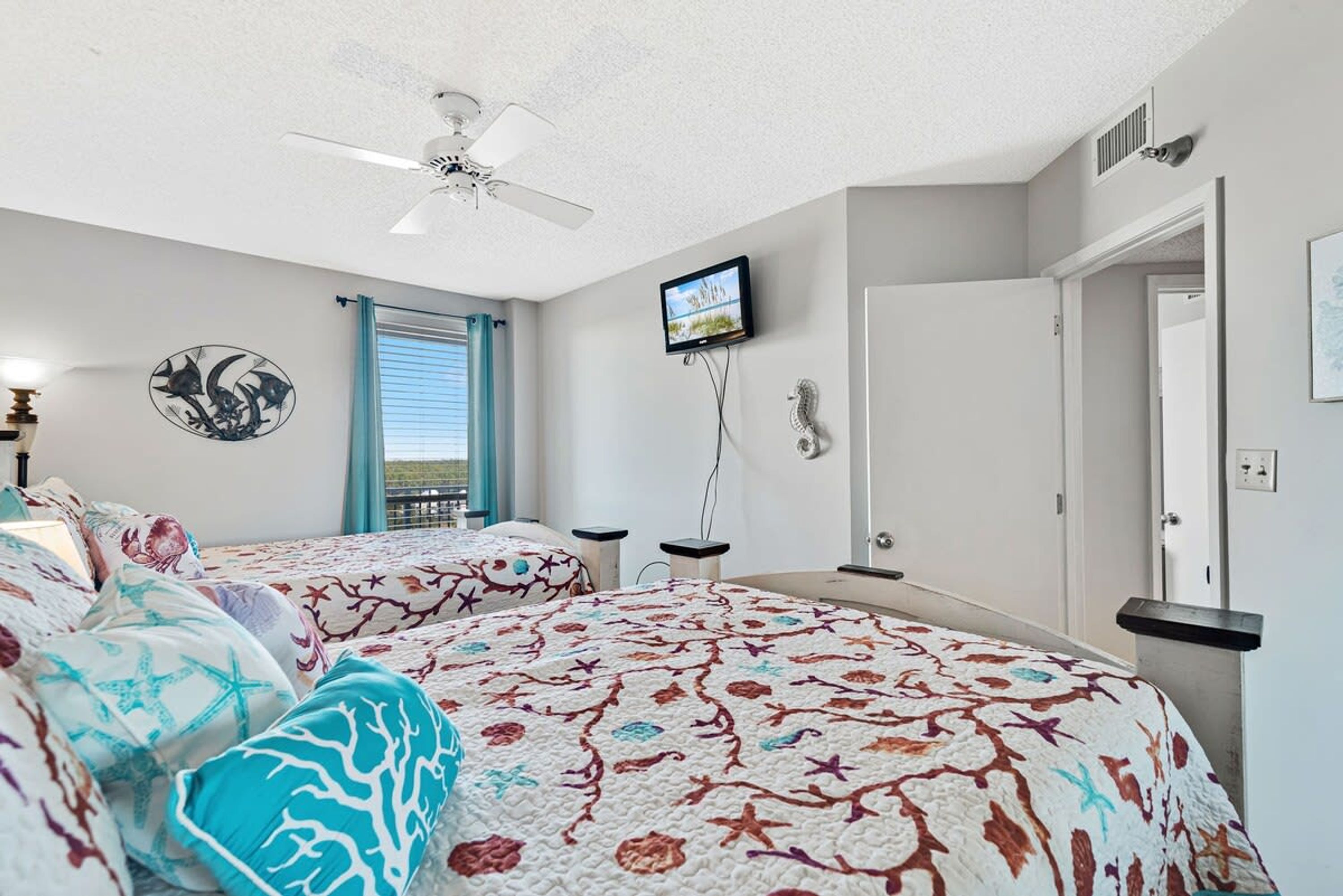 A bedroom with two beds, a ceiling fan, a TV, and a window with curtains.