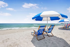A beach with blue and white beach umbrellas, wooden beach chairs, and a clear view of the ocean.
