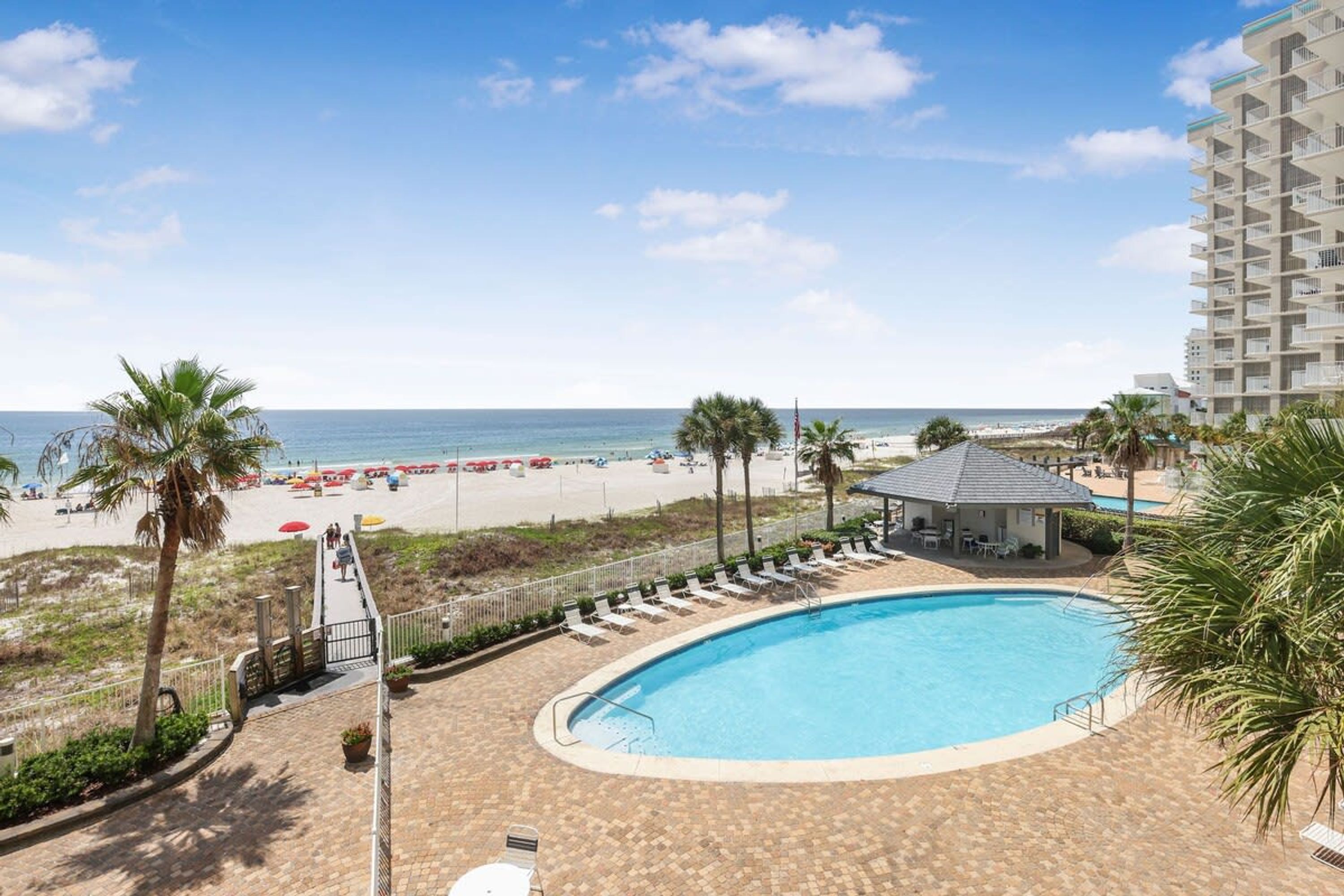 A pool area with a view of the beach and ocean, a covered seating area, and a building with balconies.