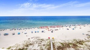 Ein Strand mit vielen Sonnenschirmen und Liegestühlen, ein sandiger Uferstreifen und das Meer im Hintergrund.