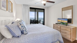 Ein Schlafzimmer mit einem Bett, einem Deckenventilator, einem Fernseher und einem Balkon mit Blick.