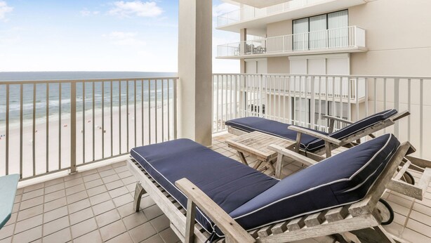 Ein Balkon mit zwei Liegestühlen und einem Tisch, mit Blick auf einen Strand.