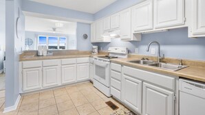 Une cuisine avec des meubles blancs, une cuisinière, un évier et un lave-vaisselle.