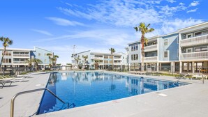 Une piscine entourée d’immeubles à plusieurs étages dotés de balcons, de palmiers et de chaises longues.