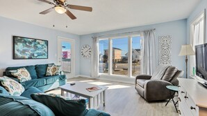 Un salon avec un canapé de couleur turquoise, un fauteuil gris, une table basse et un ventilateur de plafond.