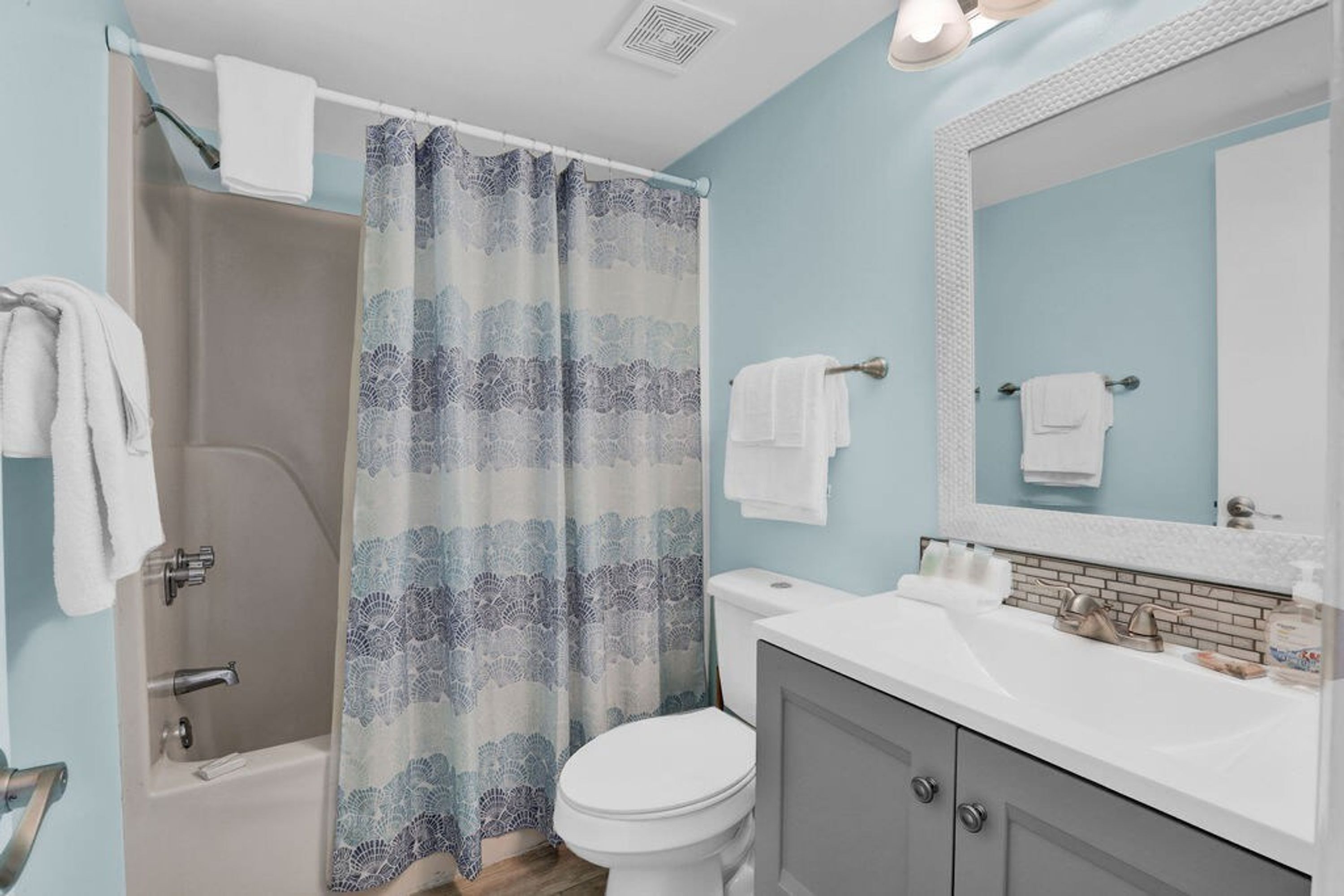 A bathroom with a shower, toilet, sink, and mirror.