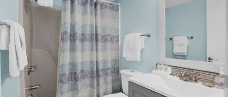 A bathroom with a shower, toilet, sink, and mirror.