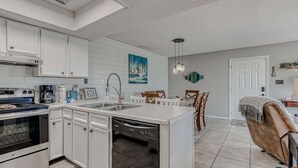 Een moderne keuken met witte kastjes, een inbouwvaatwasser en een eethoek met een witte tafel en stoelen.
