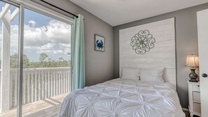 Een slaapkamer met een groot bed, uitzicht op de omgeving, een decoratief wandobject en een klein nachtkastje met een lamp.