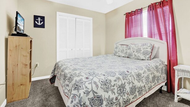 A bedroom with a bed, a wooden wardrobe, a ceiling fan, a white door, and red curtains. - Seaside Beach 5415- Beach Front Pools Sauna (Orange Beach)