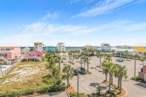 A coastal area with colorful buildings, a parking lot, and palm trees. - Sanibel 306- Beach Access Gulf Views Sun Deck (Gulf Shores)