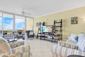 A living room with a large TV, comfortable seating, a bookshelf, and a balcony with a view. - Sanibel 306- Beach Access Gulf Views Sun Deck (Gulf Shores)