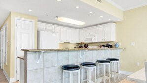 A modern kitchen with white cabinets, a granite countertop, and four bar stools. - Sanibel 306- Beach Access Gulf Views Sun Deck (Gulf Shores)