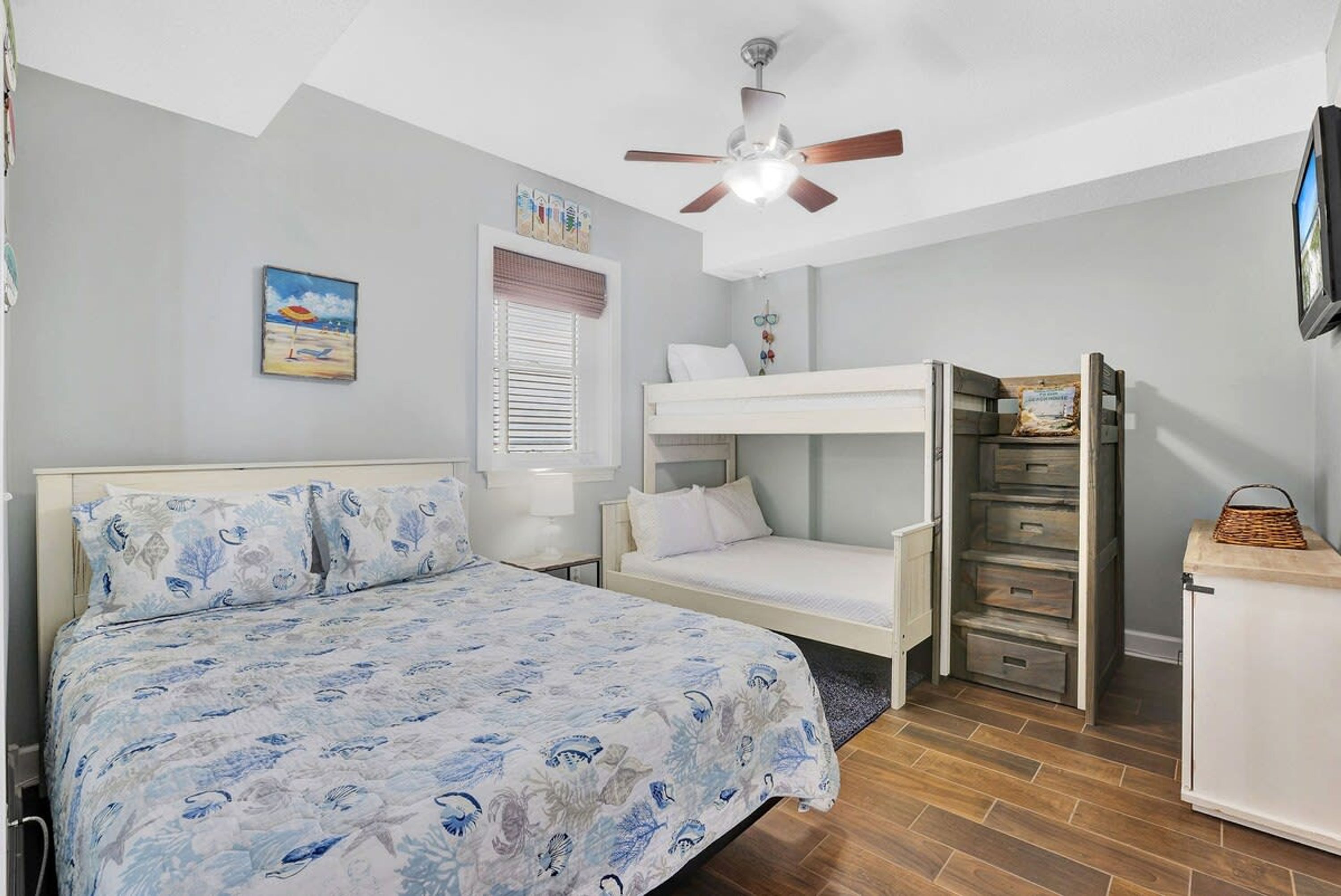 A bedroom with a bed, a ceiling fan, a window with blinds, a small desk, and a wardrobe.