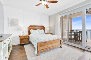 Relax in this serene bedroom with a comfortable bed, bedside tables, and a ceiling fan. Enjoy the ocean view from the sliding glass door leading to an outdoor area.