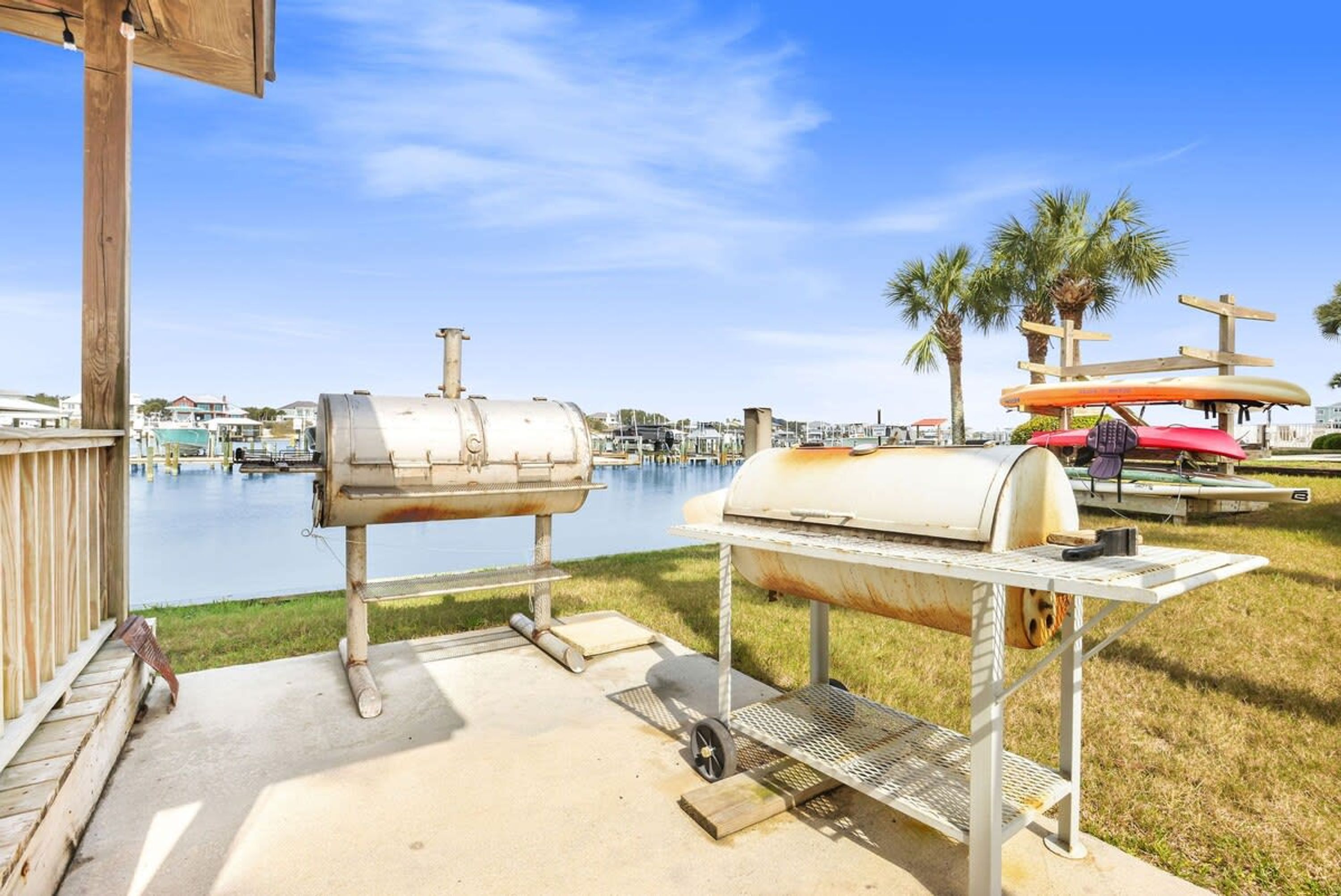 A barbecue grill set up on a concrete patio with a view of a marina and palm trees in the background.