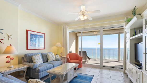 A living room with a sofa, armchairs, a coffee table, a TV, and a balcony with a view of the ocean. - Regency Isle 711 2 BR 2 5 BA Sleep 8 Gulf-front (Orange Beach)