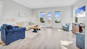 Un salón espacioso con un sofá azul, un sofá beige y un sillón azul. Hay una mesa de centro de madera y un televisor montado en la pared.