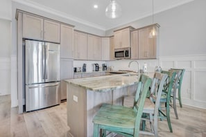 A modern kitchen with stainless steel appliances, a marble countertop, and wooden chairs.