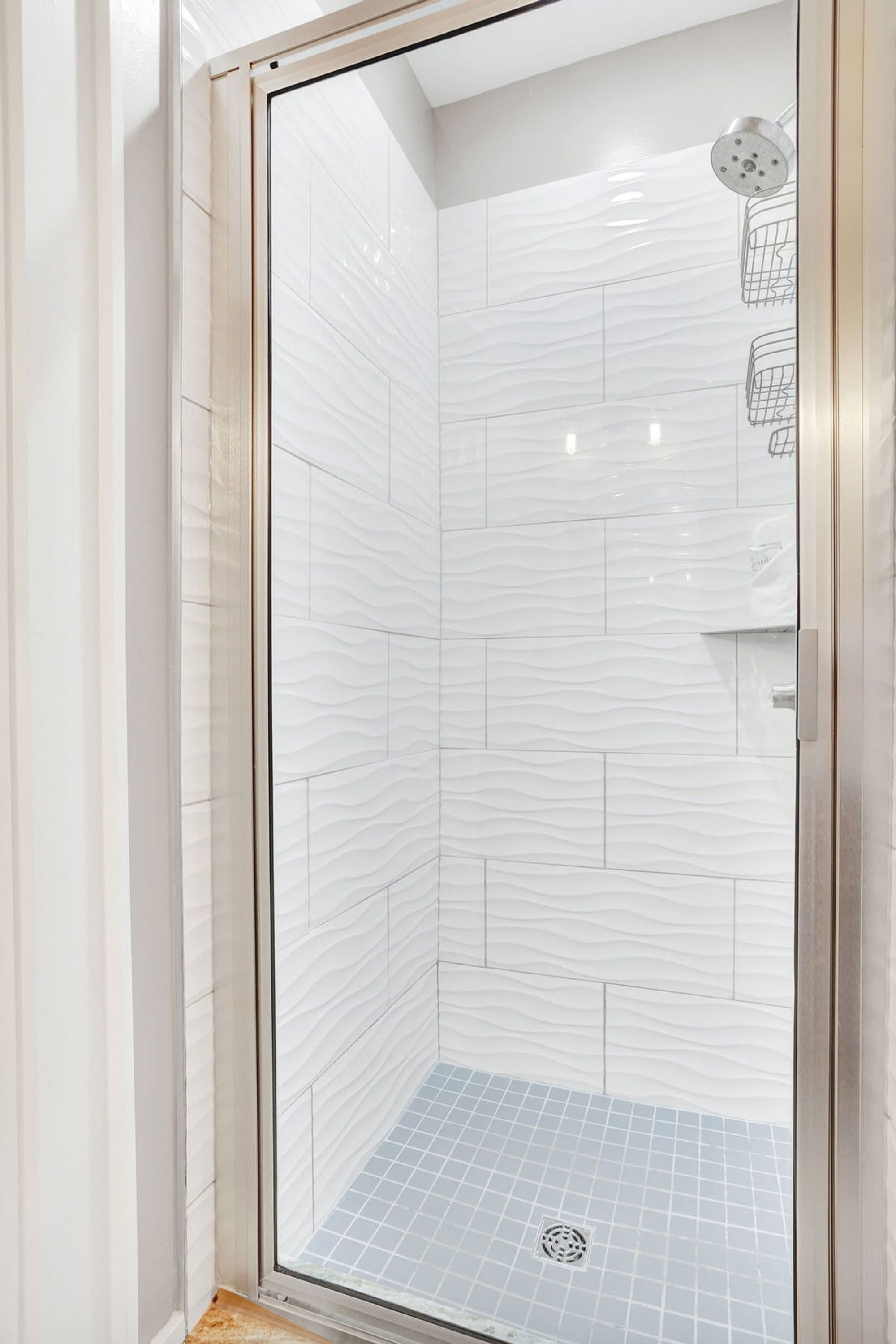 A glass-enclosed shower with white patterned tiles and a blue-tiled floor.