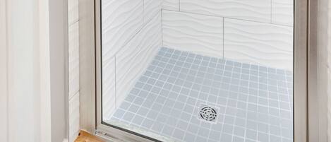 A glass-enclosed shower with white patterned tiles and a blue-tiled floor.