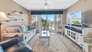 Una sala de estar con sofá, mesa de centro, televisor y un balcón con mobiliario exterior.