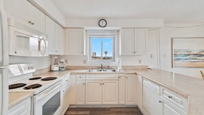 A kitchen with white cabinets, a stove, a microwave, a sink, and a window with a view. - Lei Lani 218 Best of Beach Bay (Orange Beach)