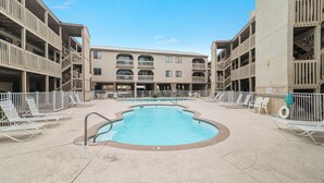A swimming pool surrounded by lounge chairs and a multi-story building with balconies.