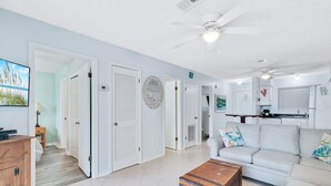 A spacious living room with a sofa, a coffee table, and a ceiling fan. There is a kitchen area with a stove and a microwave.