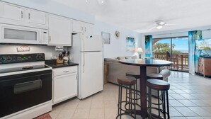 A kitchen with white cabinets, a black stove, a microwave, and a refrigerator. There is a dining area with a table and stools.