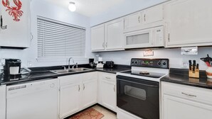 A modern kitchen with white cabinets, a black stove, a microwave, and a coffee maker.
