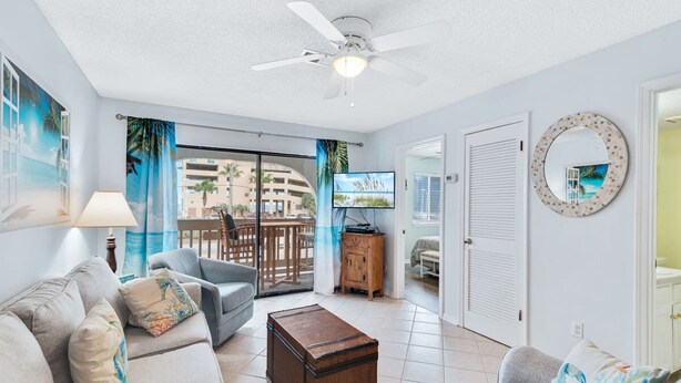 A living room with a sofa, a coffee table, a ceiling fan, and a television.