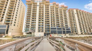 A multi-story residential building with balconies, a central entrance, and a wooden boardwalk leading to the entrance. - Phoenix II 2101-amenities Galore Beachfront (Orange Beach)