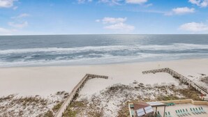 A beach with a wooden boardwalk leading to a sandy area with lounge chairs and a small building. - Phoenix II 2101-amenities Galore Beachfront (Orange Beach)