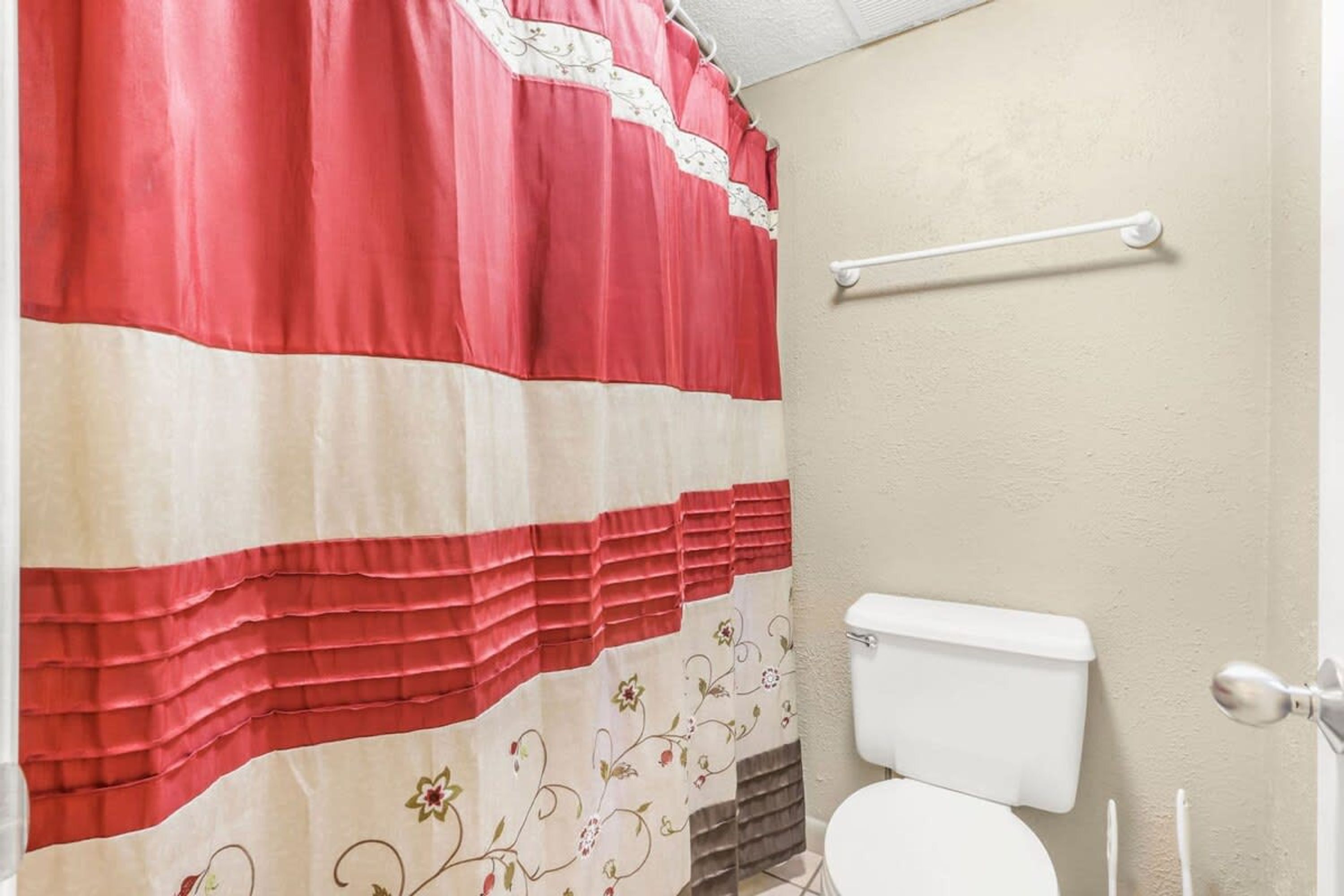 A bathroom with a toilet, a towel rack, and a shower curtain with a floral pattern.
