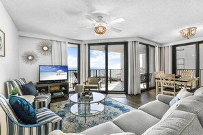 A spacious living room with a large flat-screen TV, a ceiling fan, and a balcony with a view of the ocean. - Phoenix III 3031 Beachfront End-unit (Orange Beach)